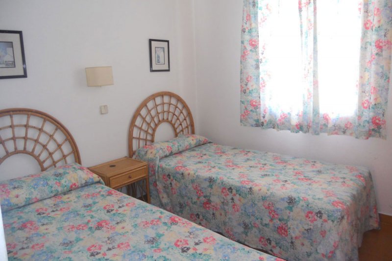 Bright bedroom with two single beds and window of the apartment Rocas Marinas 4R.