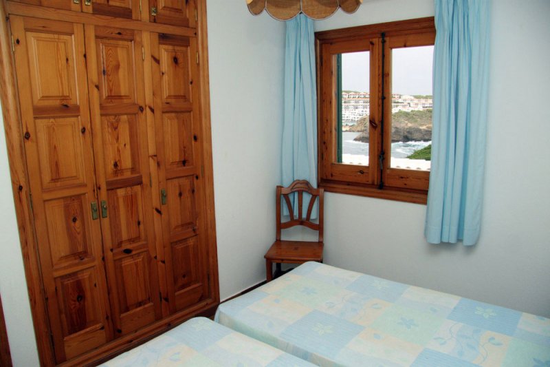 Parte del dormitorio con armario de madera y ventana.