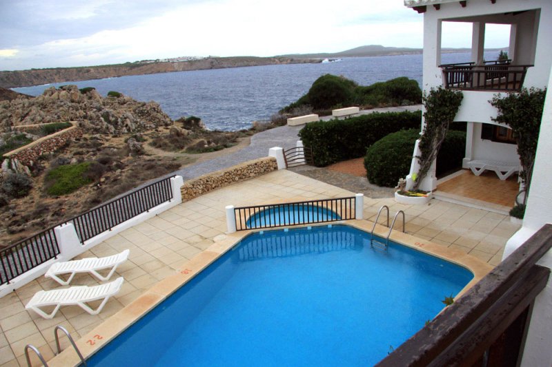 Terrace and pool of the Arco Iris apartments, and the coast of Menorca in the background.