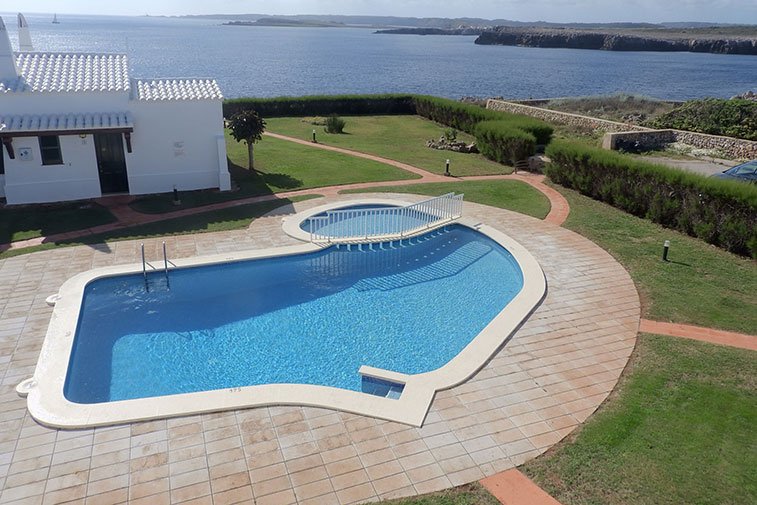 Vista superior de la piscina comunitària dels apartaments Rocas Marinas i la costa de Menorca.